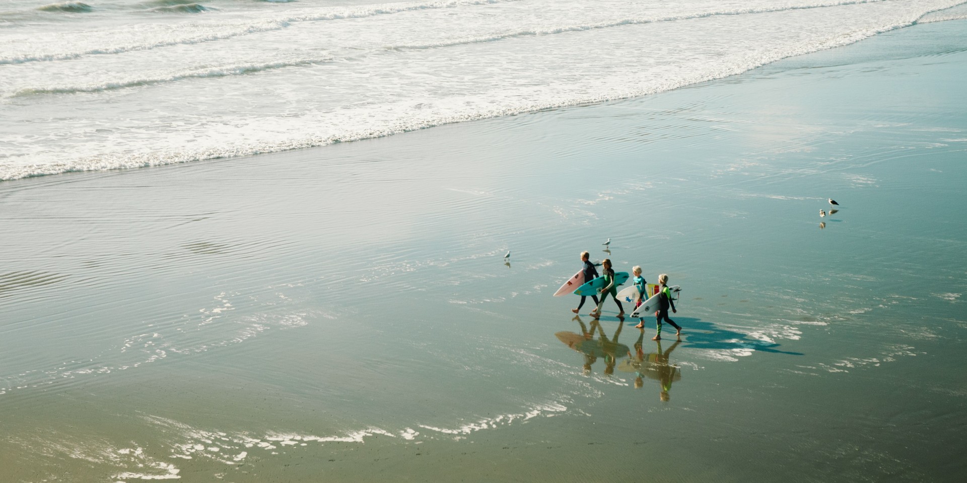 A family of surfers walking along the beach in the sun